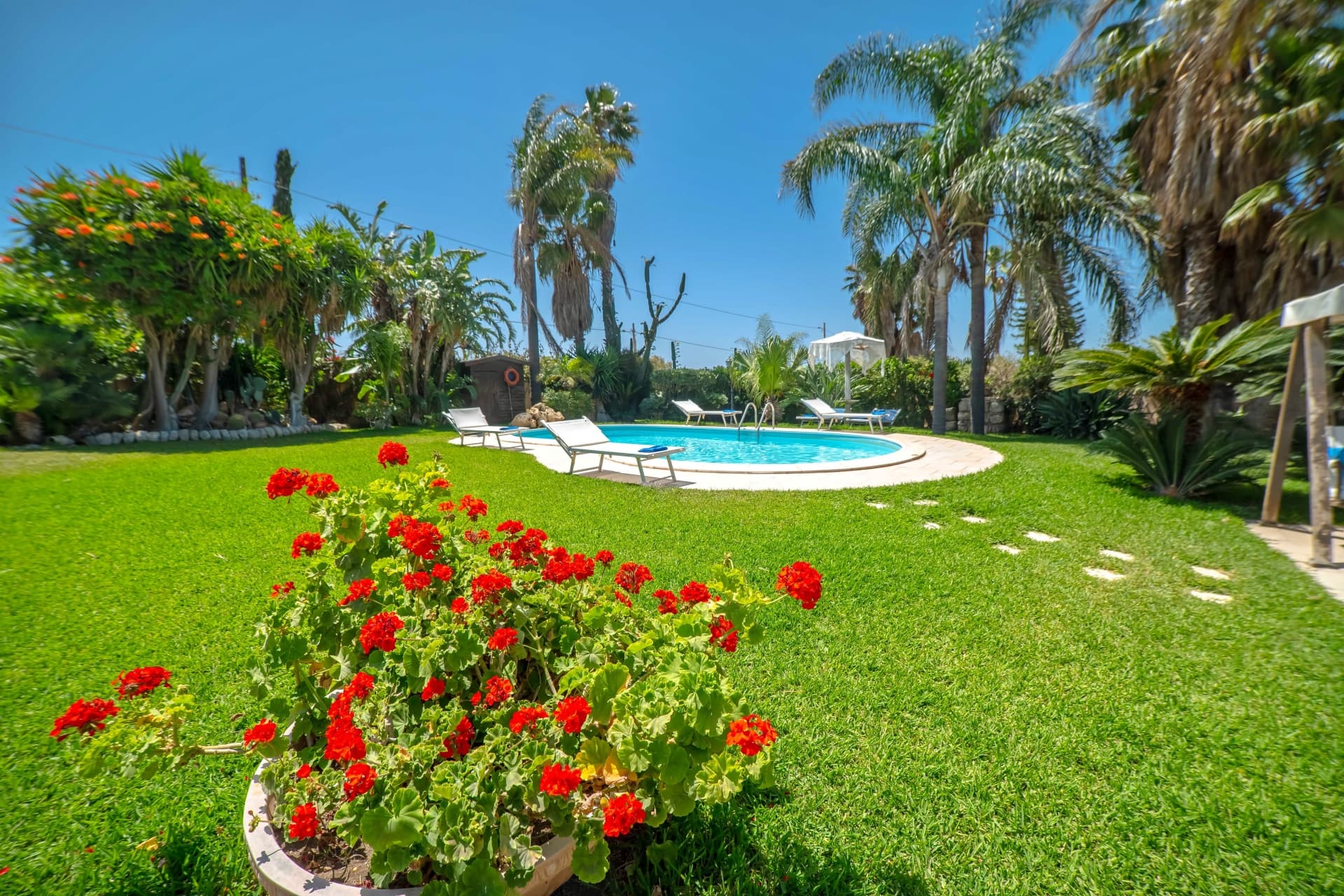 Piscina privata di giorno con prato, fiori e palme